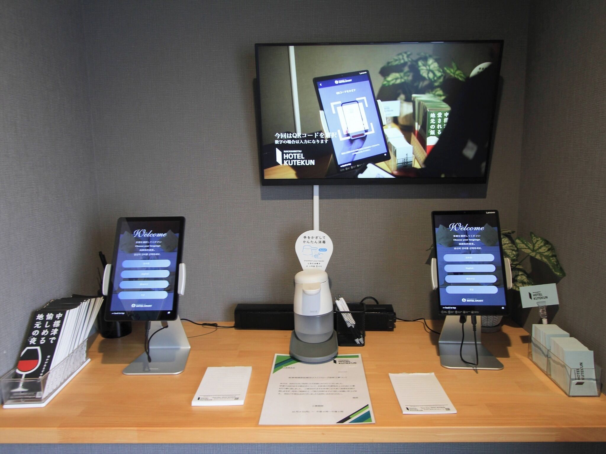 Una recepción con un mostrador que tiene dos tabletas Lenovo mostrando una pantalla de bienvenida, una cafetera y un teléfono.