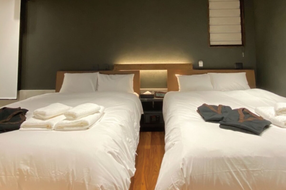 Two single beds with white linens, a wooden headboard, and a nightstand with a lamp between them.