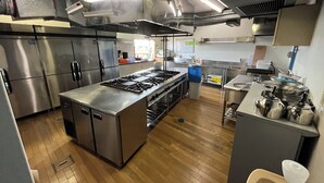 A commercial kitchen with stainless steel appliances, a central island, and a sink area. - Orando no Nikai (Aridagawa)