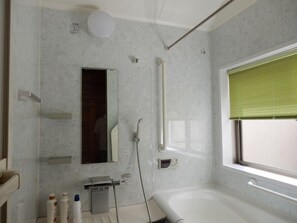 Un baño moderno con bañera, inodoro, ducha, espejo y ventana con persianas.