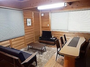 A wooden cabin interior with a sofa, a small table, a TV, and a dining table with chairs. - Yadoya Sanbou (Kyoto)
