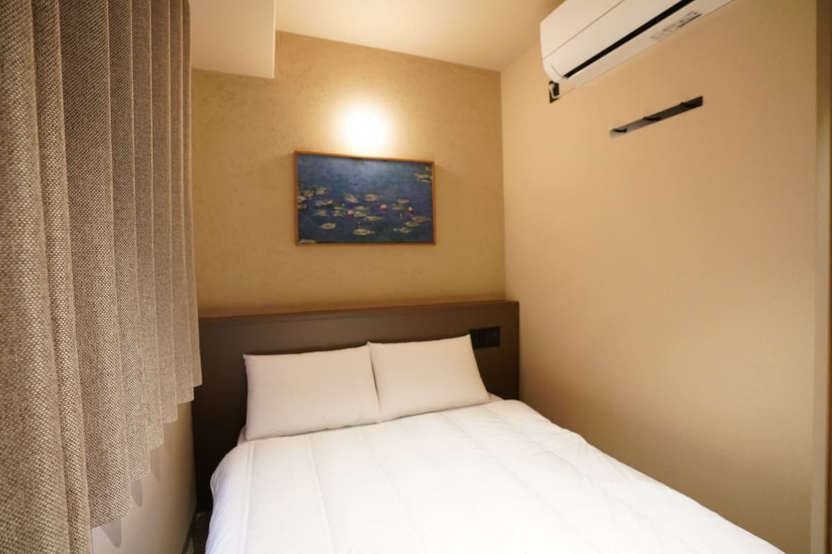 Ett hotellrum med en säng, en tavla på väggen och en luftkonditioneringsanläggning.