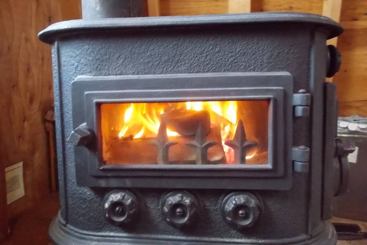 A wood-burning stove with visible flames, a control panel with two knobs, and a glass window.
