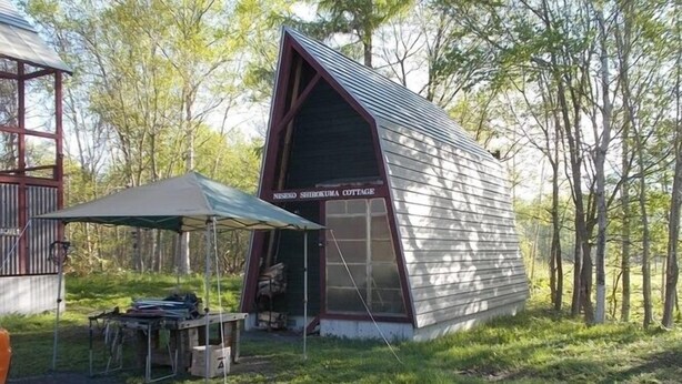 A small, wooden cabin with a pitched roof and a sign reading 'Neseko Shibokuma Cottage.' - Niseko Shirokuma Cottage (Niseko)