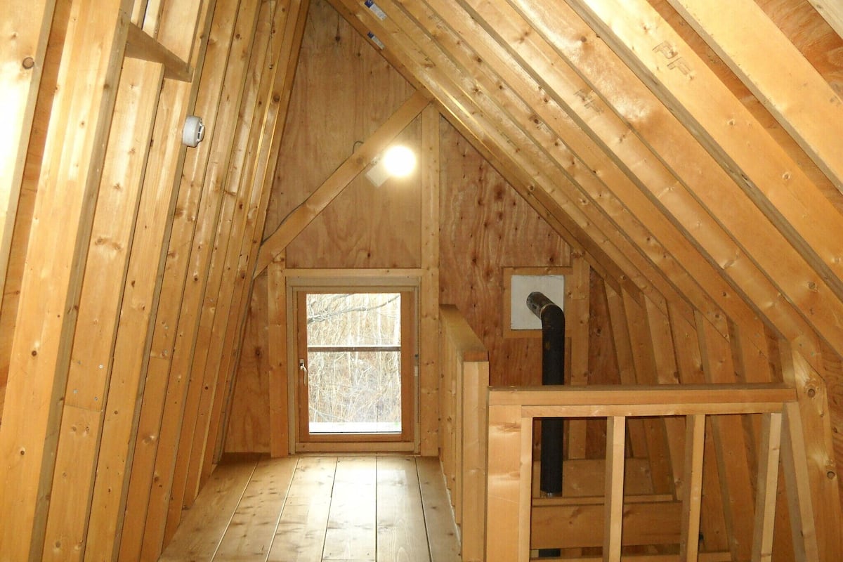 An attic room with wooden walls, a window, and a door.