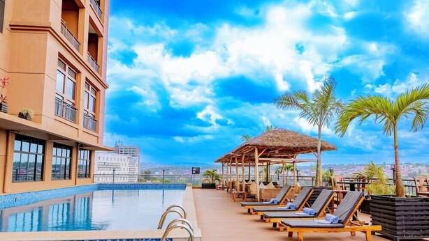 A rooftop pool with lounge chairs, a thatched-roof structure, and a view of the cityscape. - M Hotel Kigali (Kigali)