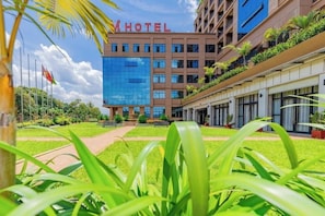 Un edificio di un hotel con una moderna facciata in vetro, un giardino curato e un cielo sereno.