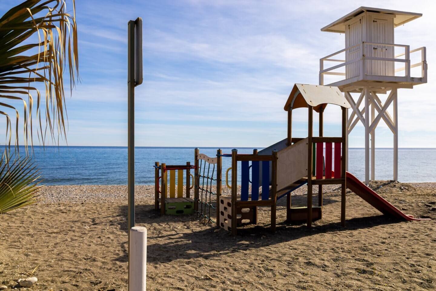 Een strand met een houten speelconstructie, een uitkijktoren voor de strandwacht en een helder uitzicht op de zee.