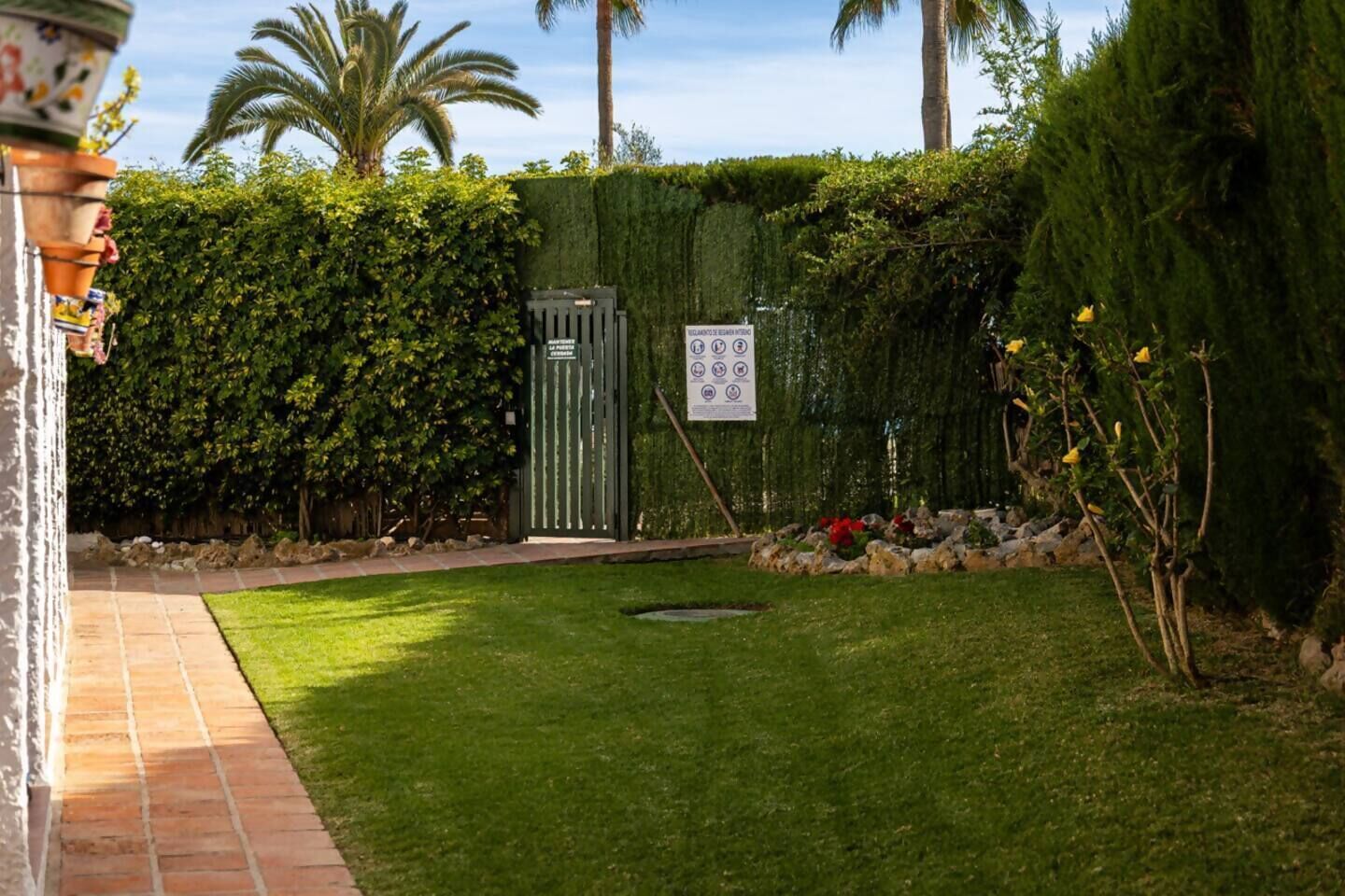Un jardín bien cuidado, césped verde, una verja metálica y un seto.