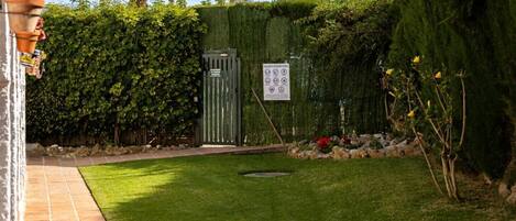 Un jardín bien cuidado, césped verde, una verja metálica y un seto.