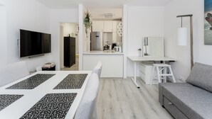 Ein modernes, kompaktes Wohnzimmer mit Flachbildfernseher, einer Küchenzeile, einem Essbereich und einer Sitzecke.