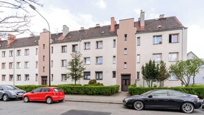 A multi-story residential building with a uniform facade, several windows, and a parking area with two cars. - Gliwice Homely Apartment (Gliwice)
