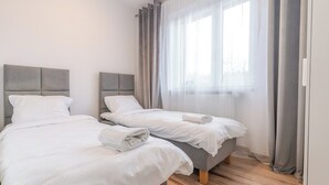A hotel room with two beds, a large window with sheer curtains, and a wooden floor. - Gliwice Homely Apartment (Gliwice)