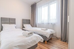 A hotel room with two beds, a large window with sheer curtains, and a wooden floor. - Gliwice Homely Apartment (Gliwice)