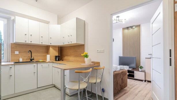 A modern kitchen with white cabinets, a wooden countertop, and a bar stool. - Gliwice Homely Apartment (Gliwice)