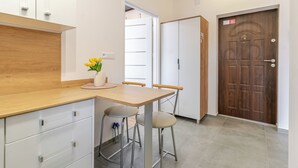 A kitchen with a wooden countertop, two stools, a vase with flowers, and a door with a sign. - Gliwice Homely Apartment (Gliwice)