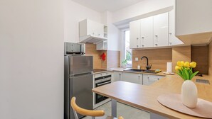 A modern kitchen with a built-in oven, a microwave, and a stainless steel refrigerator. There is a wooden countertop with a sink and a vase of yellow flowers. - Gliwice Homely Apartment (Gliwice)