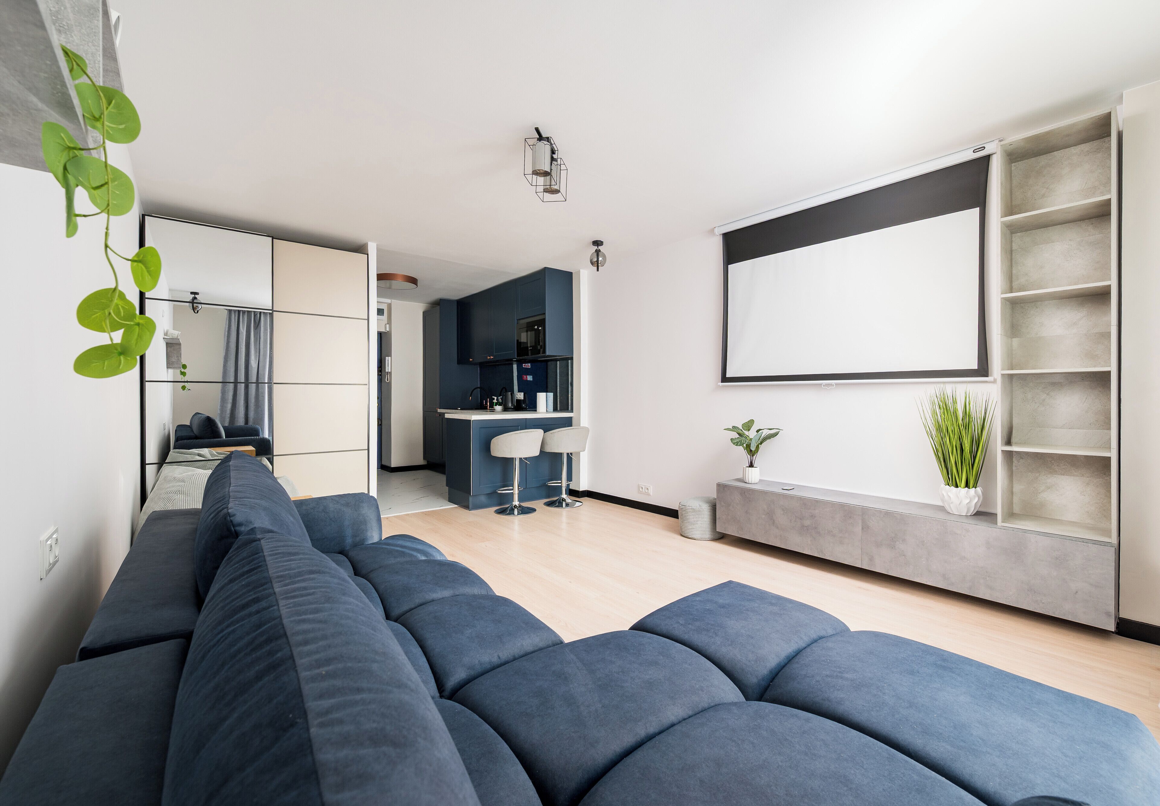 A modern living room with a sectional sofa, a kitchen area, and a large window.