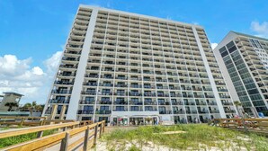 Een meerlaags hotel met balkons, uitzicht op het strand en een houten pier.