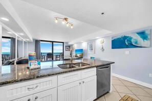 A modern kitchen with a granite countertop, white cabinetry, and a dishwasher. There is a large window offering a view of the ocean. - Gulf Front-Heart of Destin-Lots of Amenities! Sundestin 209 (Destin)