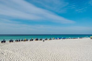 A wide sandy beach with rows of beach chairs and umbrellas, a clear blue sky, and calm sea. - Gulf Front-Heart of Destin-Lots of Amenities! Sundestin 209 (Destin)