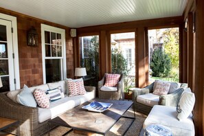 A sunlit patio with wicker furniture, a coffee table, and a view of the garden. - Quiet, private East Hampton home with pool close to Round Swamp (East Hampton)