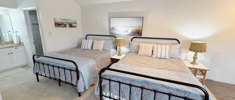 A bedroom with two beds, a ceiling fan, a painting, and a small table with a lamp.