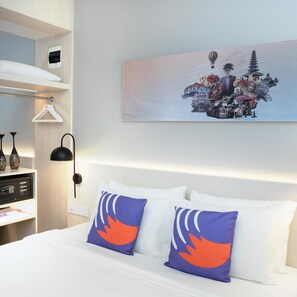 A hotel room with a bed, two pillows, a nightstand, a lamp, a wall-mounted picture, and a shelf with a remote control. - Fox Lite Hotel Samarinda (Samarinda)