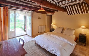 Ein Schlafzimmer mit einem Bett, zwei Nachttischlampen, einem Holztisch und Blick durch eine offene Tür.