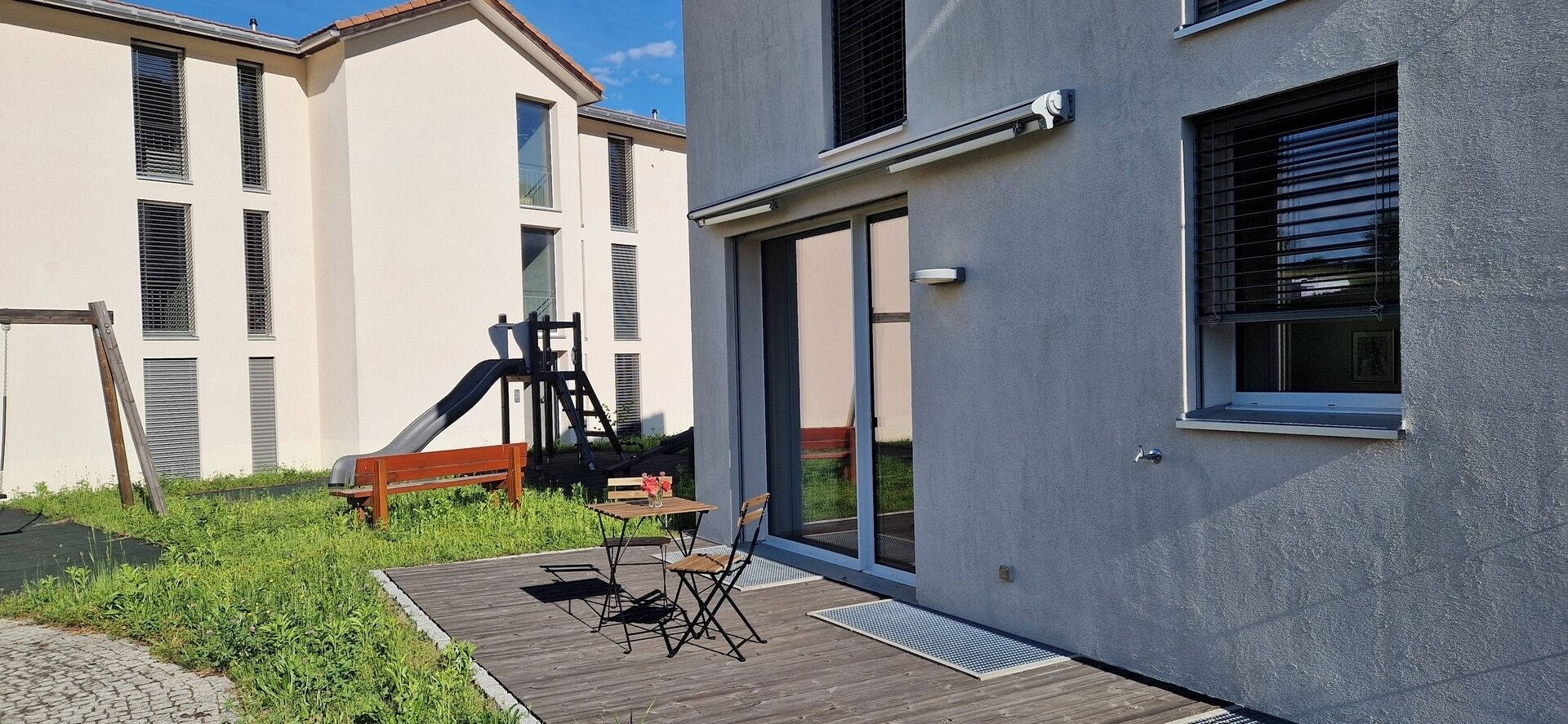 A modern building with a wooden deck, a slide, and a table with chairs.