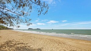 A sandy beach with gentle waves, a clear sky, and distant landforms.