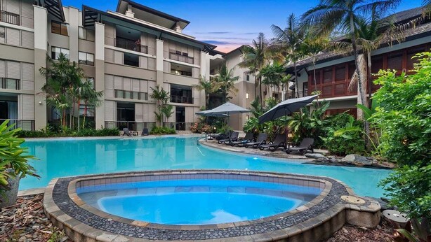 A hotel with a swimming pool, lounge chairs, and tropical plants.