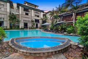 A hotel with a swimming pool, lounge chairs, and tropical plants.
