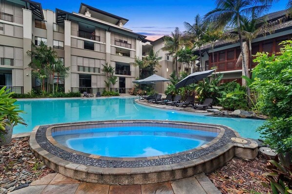 Un hotel con piscina, sillas de descanso y plantas tropicales.