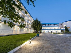 Un hotel amb un pati empedrat de pedra, un jardí ben cuidat i un arbre gran.