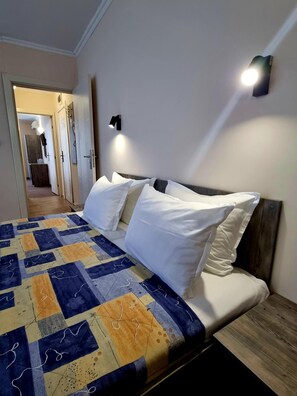 Un dormitorio con cama, mesita de noche, luz empotrada en la pared y puerta que da a otra habitación.