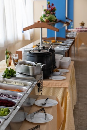 Montaje de bufé con distintas estaciones de comida, incluyendo una barra de ensaladas y platos calientes, dispuesto sobre una mesa larga.