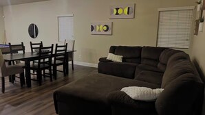 A living room with a sectional sofa, a dining table with chairs, and two wall art pieces. - The home away from home! (Bakersfield)