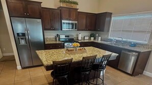 A kitchen with a granite countertop, stainless steel appliances, and a bar area with stools. - The home away from home! (Bakersfield)