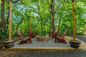 A circular seating area with a fire pit, surrounded by wooden chairs and potted plants, set in a forested area. - NEW Hot Tub • 2 Mi to Parkway • Fire Pit • Arcade (Sevier County)