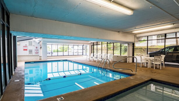 An indoor swimming pool with clear water, a lifeguard station, and a seating area with chairs and tables. - King 1BR Retreat, Jetted Bathtub, Indoor + Outdoor Pool, Walk to Parkway (Gatlinburg)