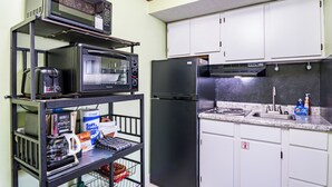 A kitchen with a microwave, toaster, refrigerator, and a shelf with various items. - King 1BR Retreat, Jetted Bathtub, Indoor + Outdoor Pool, Walk to Parkway (Gatlinburg)