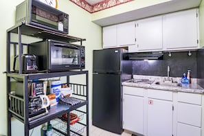 A kitchen with a microwave, toaster, refrigerator, and a shelf with various items. - King 1BR Retreat, Jetted Bathtub, Indoor + Outdoor Pool, Walk to Parkway (Gatlinburg)