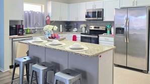 Een moderne keuken met witte kasten, roestvrijstalen apparatuur en een centraal eiland met krukken.