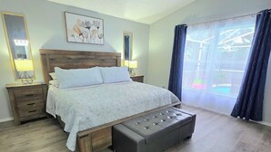 Een slaapkamer met een houten bed, nachtkastjes, een spiegel, een raam met gordijnen en uitzicht op groen.