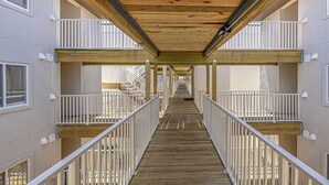A wooden deck connecting multiple floors of a building with white railings and a clear view of the outside. - Coastal Condo with Partial Ocean View | Walk to East Beach | Pool + Grills (Saint Simons Island)