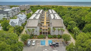 A multi-story hotel with a central atrium, parking lot, and pool area. - Coastal Condo with Partial Ocean View | Walk to East Beach | Pool + Grills (Saint Simons Island)