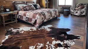 Una habitación rústica con una cama de madera, un tapiz de cuero de vaca, un armario de madera y una ventana con cortinas.