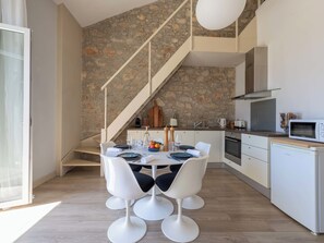 Eine moderne Küche mit Steinwand, weißen Schränken und einem Essbereich mit weißen Stühlen und einem runden Tisch.