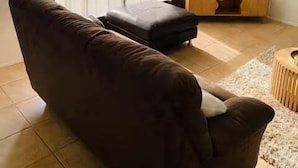 A living room with a sofa, a television on a wooden stand, and a large window with curtains. - Pet Friendly Coastal Stay Near The Beach. (Bundaberg)